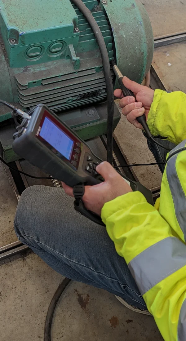 Technician taking a vibration measurement on an electric motor using a handheld analyser and a contact accelerometer